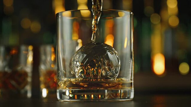 Super Slow Motion Shot of Pouring Whiskey into Glass with Ice Sphere in Bar at 1000fps.