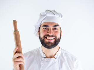 Young male chef showing a wooden rolling pin while smiling and looking at camera. Isolated on a white background