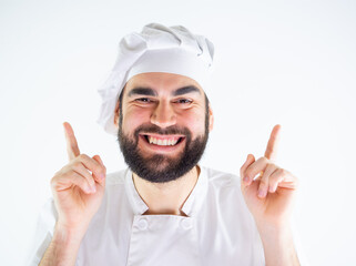 Young male chef pointing up with both hands while smiling and looking at camera. Isolated on a white background