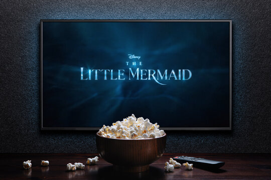 TV screen playing The Little Mermaid trailer or movie. TV with remote control and popcorn bowl. Moscow, Russia - March 20, 2023.