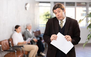 Adult man in business suit posing with documents in his hands in office space