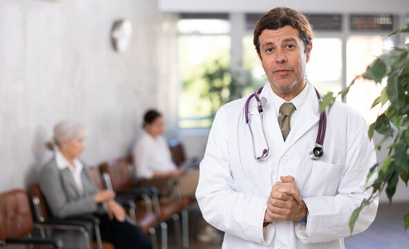 male medical eceptionist affably waiting for patients of clinic in waiting room