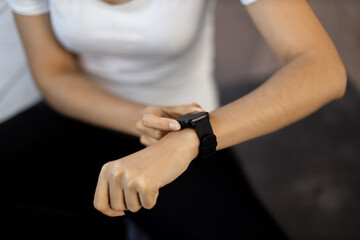 Close-up of young sporty woman resetting heart-rate watch on her wrist while sitting on yoga mat. Activity tracker for home training assisting fit athletic lady in meeting fitness objectives on time.