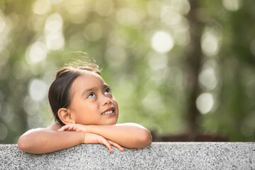 Portrait of thoughtful cute little asian girl outdoors looking up enjoying nature thinking happy thoughts