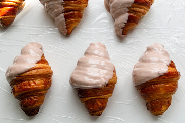 Rows of croissants are half covered with white chocolate in a bakery. Pastry decoration