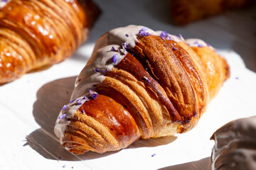 Violet-flavored croissant half covered in white chocolate. Beautifully decorated croissant in the bakery