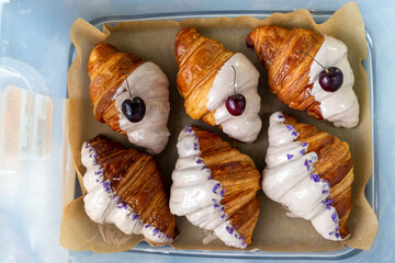 Violet-flavored and cherry-flavored croissants half covered in white chocolate packed in a box for delivery from the bakery