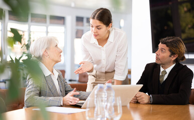 Focused interested young woman talking to male and female business partners during negotiations at table in modern office