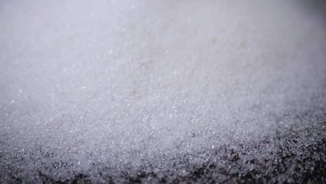 White Crystals of Granulated Sugar Fall on a Black Background in Slow Motion. Close-up. Stream of sugar particles pours down, fills surface. Granules. Texture, abstract background. Sugar consumption.