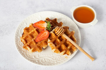 Belgian liege waffles with strawberries and honey on a light table