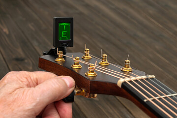 Hand tuning a guitar with a tuner. Close up.