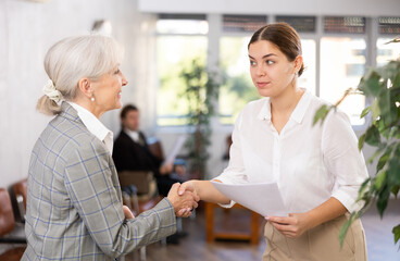 Fototapeta premium Young woman shaking hands with mature colleague after making changes to expense document. Female coworker s handclasp was strong and friendly