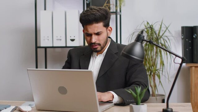 Irritated shocked indian business man while working on laptop, unexpected online website problem, computer virus data loss by hacking. Freelancer feeling mad about broken notebook at office workplace
