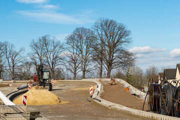 Construction site for laying the road surface with an excavator standing on it and a pile of sand...