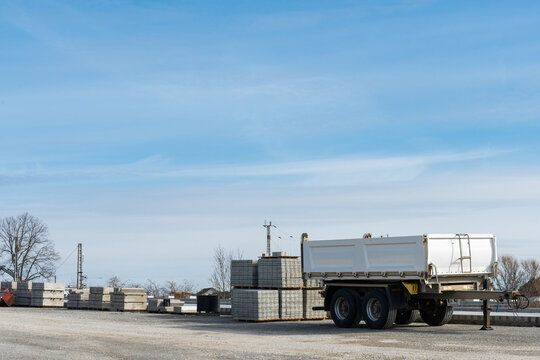 Construction site with empty car trailer and building materials stacked on pallets. Blue sky with light white clouds.