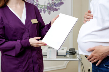 An obstetrician-gynecologist holds a patient card in his hands. A pregnant woman at an appointment with a gynecologist. The patient talks to the doctor after cardiotocography.