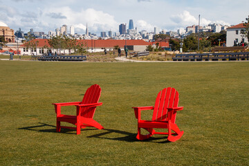Two red chairs are sitting on green grass at The Presidio's Tunnel Top Park. In the background is...