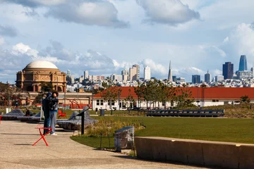 Fotobehang A view of the San Francisco skyline from the Tunnel Top park in The Presidio. Two people are standing to the side. There white clouds in a blue sky. © Timothy