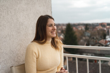 Smiling young woman sitting in terrace on rainy day and drinking tea.