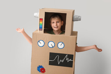 Little boy in cardboard robot costume near light wall