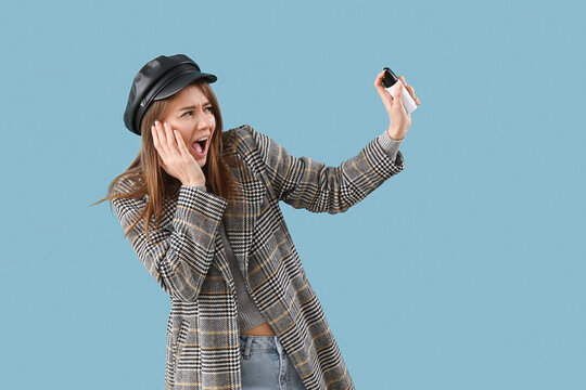 Scared young woman with pepper spray for self-defence on blue background