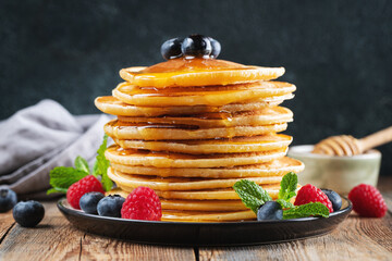 Delicious pancakes, with fresh blueberries, raspberry and maple syrup or honey on a dark background
