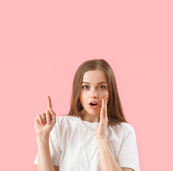 Shocked young woman pointing at something on pink background, closeup