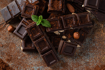 Dark and milk chocolate with nuts on a dark background sprinkled with cocoa powder.