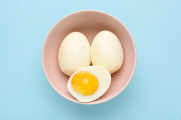 Bowl with delicious boiled eggs on blue background