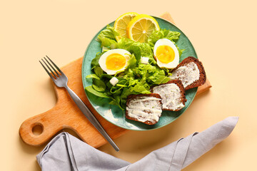 Plate of delicious salad with boiled eggs and cream cheese sandwiches on beige background