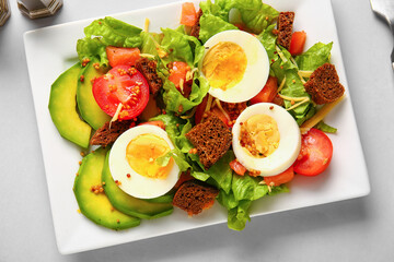 Plate of delicious salad with boiled eggs and salmon on grey background