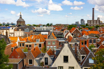 View from above of historic center of Dutch city of Leiden on sunny day overlooking typical townhouses with terracotta tiled gabled roofs, dome of St. Mary church and power station at background..