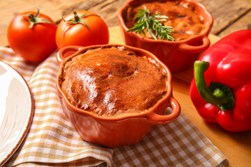 Board with delicious meat pies in baking forms and vegetables on wooden table