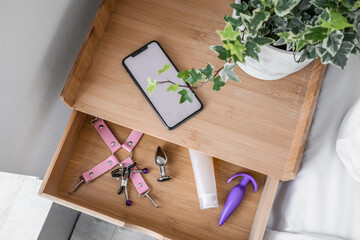 Open drawer with sex toys and mobile phone in bedroom