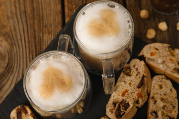 Slate board with delicious biscotti cookies and cups of coffee on wooden background