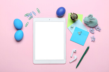 Tablet computer with office stationery, Easter eggs, rabbit and flowers on pink background