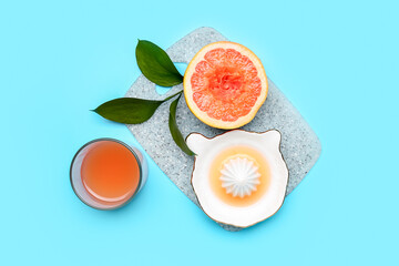 Board with ripe grapefruit, juicer and glass of juice on color background