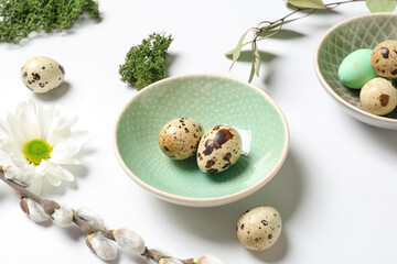 Plate with Easter quail eggs and chamomile flower on white background
