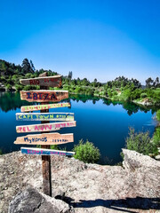 Tourism signs showing world cities in a tourist landscape in front of a lake. Wooden plaque in a tourist place showing the distance of tourist cities in the world.