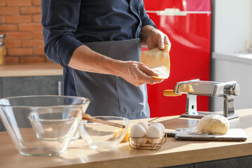 Man making pasta with machine at table in kitchen, closeup