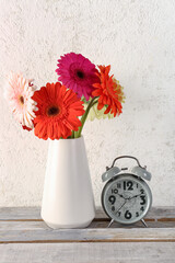 Alarm clock and vase with beautiful gerbera flowers on white grunge background