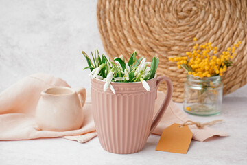 Cup with beautiful snowdrops on grey table