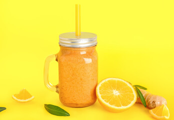 Mason jar of healthy orange smoothie with straw on yellow background