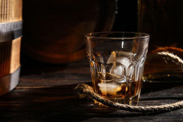 Glass of cold whiskey and rope on dark wooden background