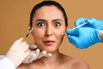 Young woman receiving filler injections in face against beige background