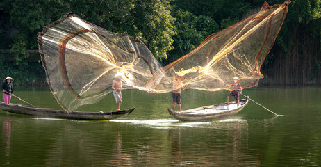 Vietnamese fishermen catching fish and throwing out two large yellow fishnet on a boat from the...