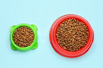 Bowls of dry pet food on color background