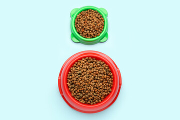 Bowls of dry pet food on color background