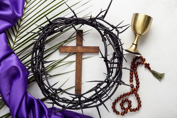 Wooden cross with crown of thorns, prayer beads, wine cup and palm leaf on white background. Good Friday concept