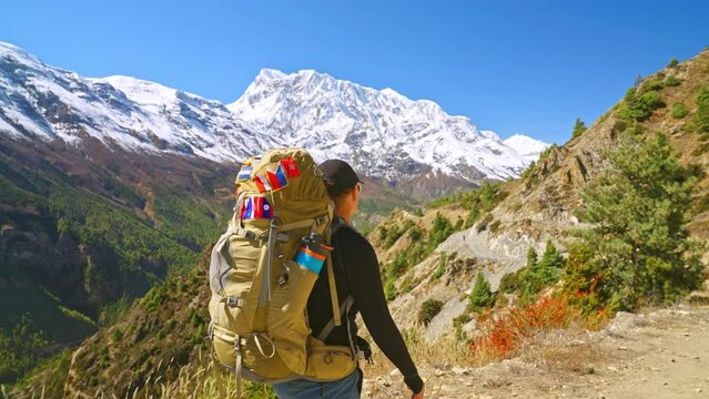 Backpacking woman traveler walking and hiking on trail while enjoying beautiful mountain landscape in the distance, Annapurna Circuit Trek, Nepal